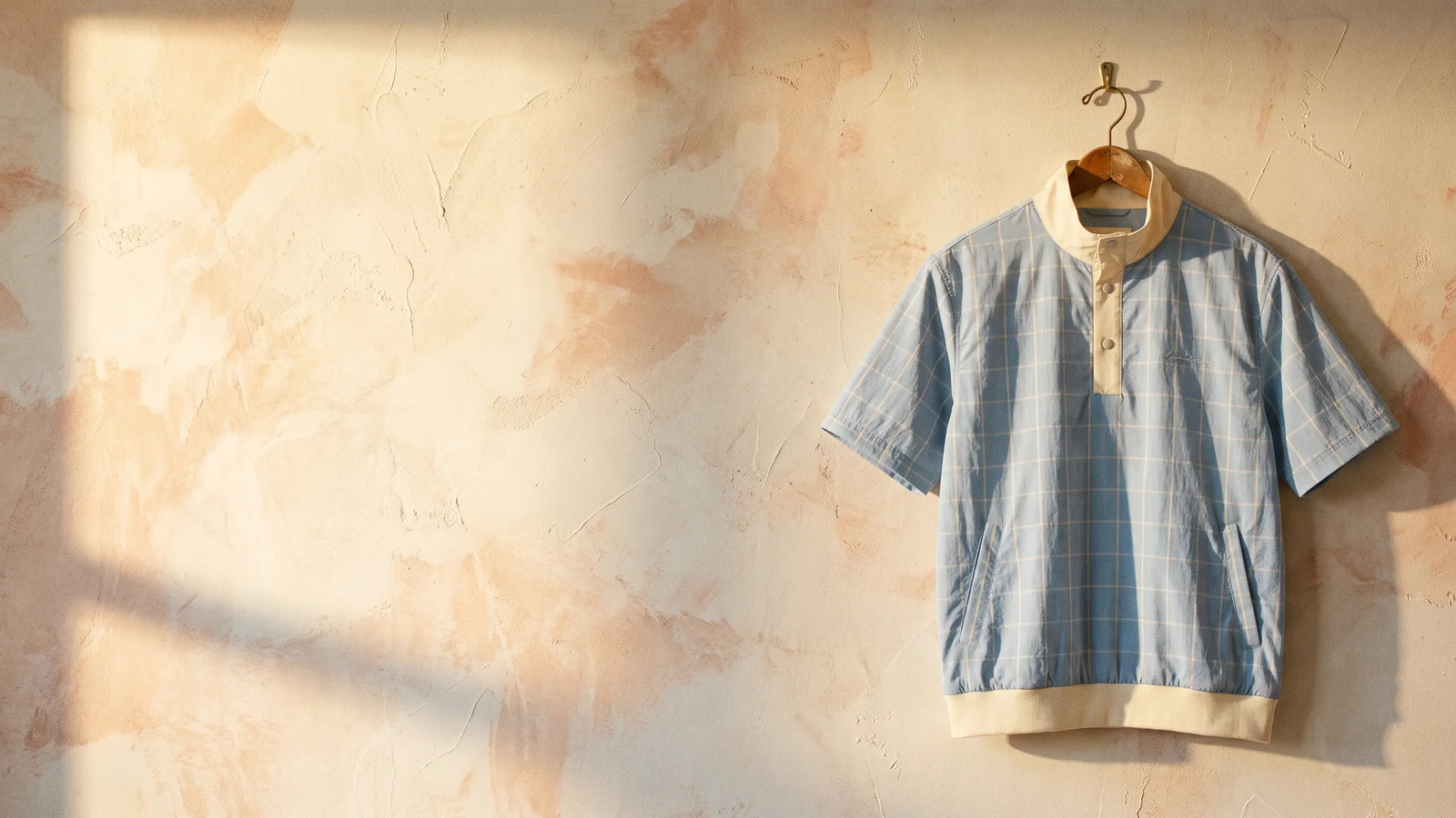 Chipper hero - powder blue windowpane wind shirt on a wooden hanger against a warm plaster wall