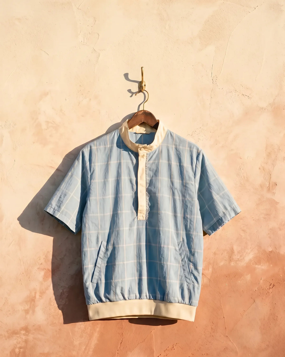 Chipper hero mobile - powder blue windowpane wind shirt on a brass hook against a warm plaster wall